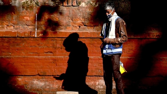 =A worker looks at his mobile as he stands on a footpath near a construction site in New Delhi.(AFP)