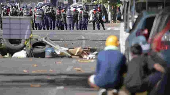 Demonstrators take shelter behind a barricade and some vehicles as riot police officers stand in front of them during a protest against the military coup in Yangon, Myanmar, on March 1. (Reuters) Demonstrators take shelter behind a barricade and some vehicles as riot police officers stand in front of them during a protest against the military coup in Yangon, Myanmar, on March 1. (Reuters)