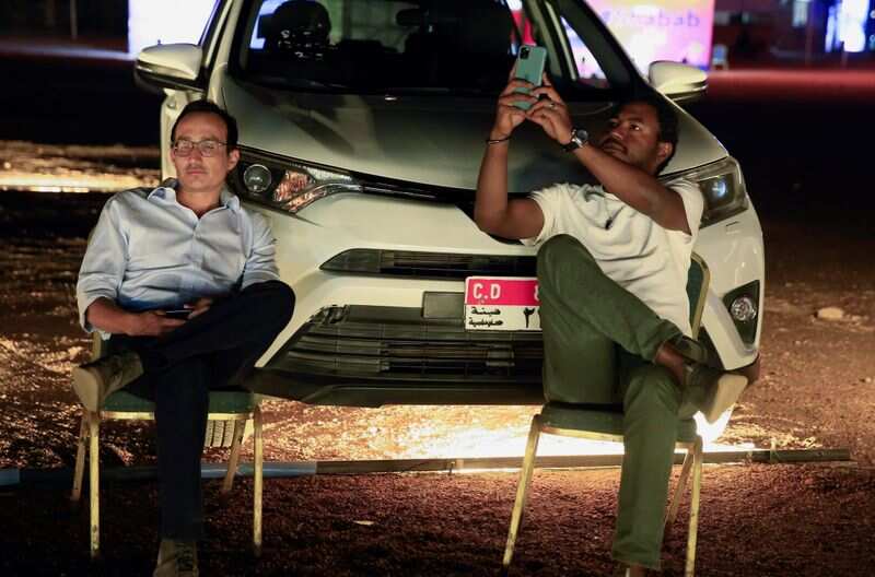 Men sit near a car as they watch a screening of the Sudanese European Film Festival at an outdoor, drive-through cinema for visitors, adhering to coronavirus disease (COVID-19) restrictions, in Khartoum, Sudan February 28, 2021. Picture taken February 28, 2021. REUTERS/Mohamed Nureldin Abdallah (REUTERS)