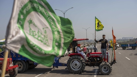 A farmer with a farm union flag stands on a tractor while blocking a highway along the Delhi-Haryana border near New Delhi on March 6. Another concern is the dismantling of the "mandi" (wholesale market) systems through the new laws. Prime Minister Narendra Modi has also assured the farmers that the MSP system would continue.(Altaf Qadri/AP)