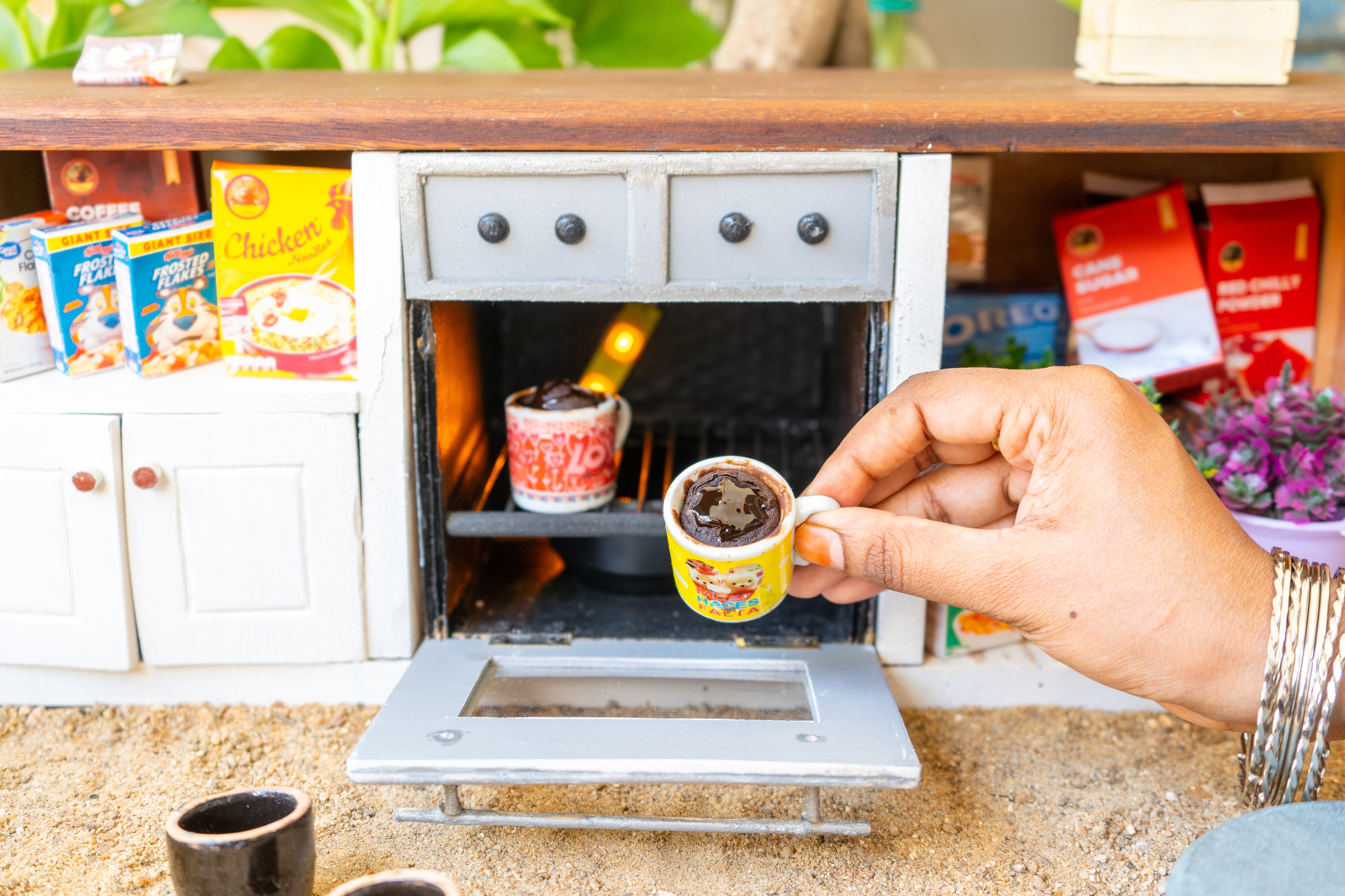 The mug cake is made in an oven fitted into a kitchen stacked with miniature cereal and biscuit boxes. The mug cake is made in an oven fitted into a kitchen stacked with miniature cereal and biscuit boxes.