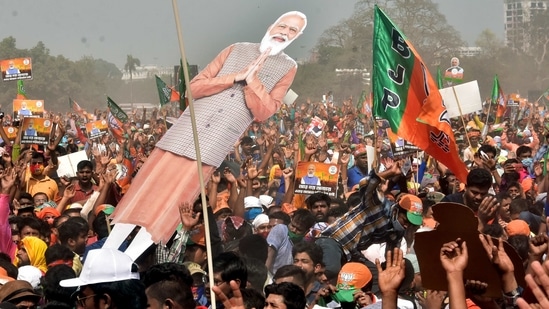 Supporters gather with the flags, posters, and an image of PM Modi during his rally ahead of the West Bengal Assembly Election in the Brigade Parade Ground in Kolkata on Sunday. (ANI Photo)