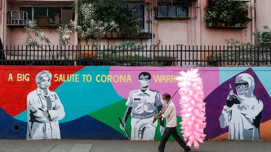 A cotton candy seller walks past a graffiti honouring the frontline workers in fight against Covid-19, on a street in Navi Mumbai on Monday.(Reuters Photo)