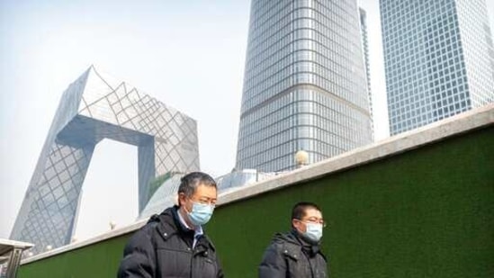 People wearing face masks to protect against the spread of the coronavirus walk past a wall surrounding a construction site for skyscrapers in the central business district in Beijing.(AP) People wearing face masks to protect against the spread of the coronavirus walk past a wall surrounding a construction site for skyscrapers in the central business district in Beijing.(AP)