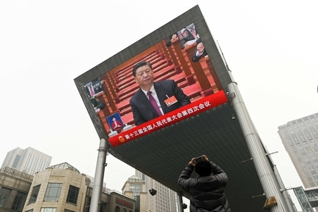 A man uses his mobile phone to take a picture of a big screen showing China's President Xi Jinping attending the opening session of the National People's Congress (NPC) at the Great Hall of the People in Beijing. (AFP)