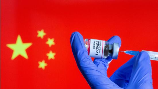 FILE PHOTO: A woman holds a small bottle labeled with a "Coronavirus COVID-19 Vaccine" sticker and a medical syringe in front of displayed China flag (REUTERS) (REUTERS)