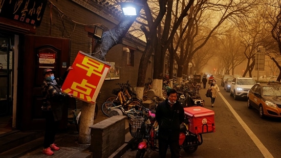 A woman hangs a sign outside a shop during the morning rush hours in Beijing, on March 15. Hundreds of flights were cancelled due to the sandstorm and the city government ordered schools to cancel outside sport and events and advised the public to stay inside where possible.(Thomas Peter / REUTERS)