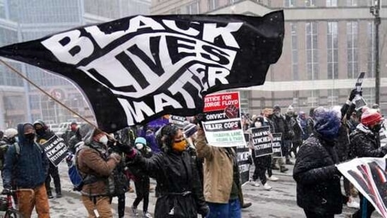 A group of protesters march in the snow around the Hennepin County Government Center, Monday, March 15, 2021, in Minneapolis where the second week of jury selection continues in the trial for former Minneapolis police officer Derek Chauvin. (AP Photo/Jim Mone)