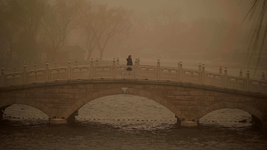 A woman walks along a bridge at Houhai lake during the sandstorm in Beijing, on March 15. A 2019 study published in the journal Nature Sustainability found some two million square miles of vegetation had been added to the surface of the earth since 2000, a quarter of which was contributed by China, AFP reported.(Noel Celis / AFP)