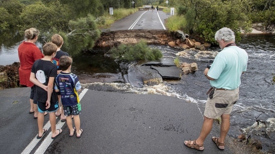 People stand at a washed-out section of road at Port Stephens, 200 kilometres north of Sydney on March 20. Record rains over the weekend have brought about the worst flooding in half a century in some areas, authorities said on March 21, forcing thousands to evacuate and damaging hundreds of houses, Reuters reported.(Mark Baker / AP)