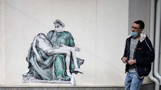 A man walks past a poster, illustrating a medic in a replica of Michelangelo's Pieta, placed on a wall near vaccination centre at Pirogov hospital, amid the spread of the coronavirus disease (Covid-19), in Sofia, Bulgaria.(Reuters)