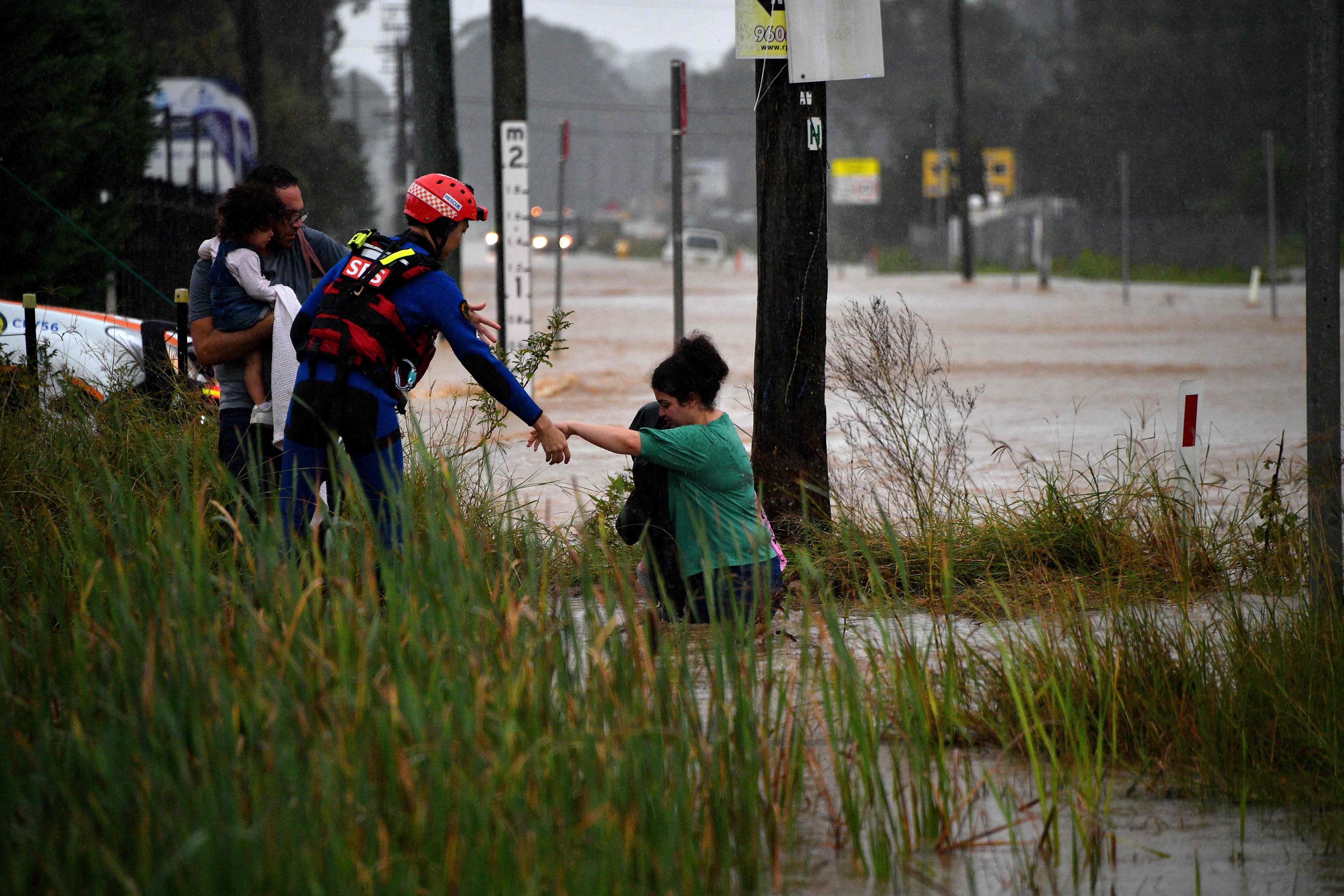 A rescue worker helps residents cross a flooded road during heavy rain in western Sydney.(AFP) A rescue worker helps residents cross a flooded road during heavy rain in western Sydney.(AFP)