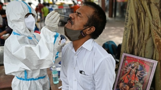 A health worker wearing protective gear collects a swab sample from a man for the Covid-19 coronavirus rapid antigen test (RAT) next to a picture of Hindu deity placed under a tree along the roadside in New Delhi on March 23, 2021.(AFP)