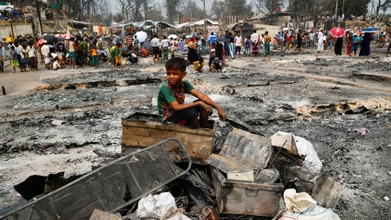 A Rohingya refugee boy sits on a stack of burned material after a massive fire broke out and destroyed thousands of shelters in a Rohingya refugee camp in Cox's Bazar, Bangladesh.(Reuters)