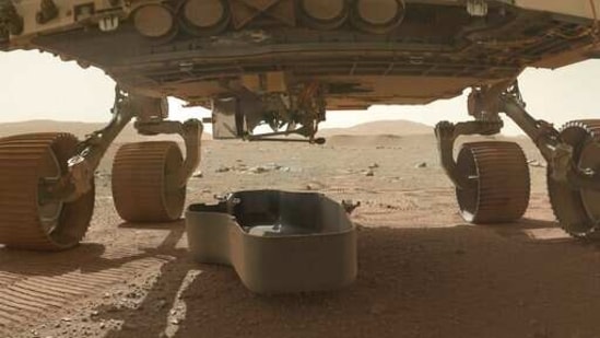 This photo made available by NASA shows the released debris shield, center, for the Ingenuity helicopter, dropped on the surface of Mars from the bottom of the Perseverance rover.(AP) This photo made available by NASA shows the released debris shield, center, for the Ingenuity helicopter, dropped on the surface of Mars from the bottom of the Perseverance rover.(AP)
