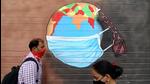A man and a woman wearing protective face masks walk past a graffiti on a wall. (REUTERS) A man and a woman wearing protective face masks walk past a graffiti on a wall. (REUTERS)