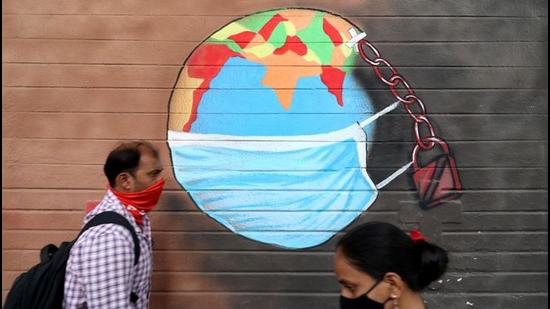 A man and a woman wearing protective face masks walk past a graffiti on a wall. (REUTERS)