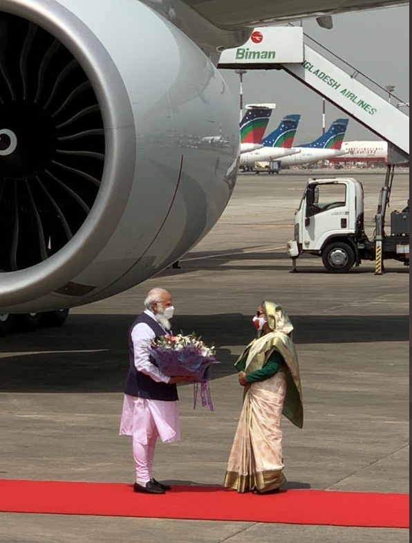 A masked Sheikh Hasina was seen greeting PM Modi with a bouquet of flowers as he alighted onto the runway. (ANI) (ANI) A masked Sheikh Hasina was seen greeting PM Modi with a bouquet of flowers as he alighted onto the runway. (ANI) (ANI)