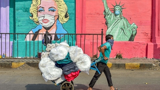 A porter walks past a mural depicting Marilyn Monroe and 'The Statue of Liberty wearing face masks, to spread awareness on COVID-19 precautions, in Mumbai, Friday, March 26, 2021. (PTI)
