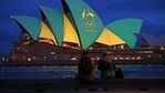A couple sit on a dock to look at the sails of the Sydney Opera House that are illuminated with the green and gold colors of the Australian Olympic team. (AP)