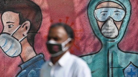 A pedestrian walks past a wall mural depicting frontline Covid-19 coronavirus warriors wearing face masks along a road.