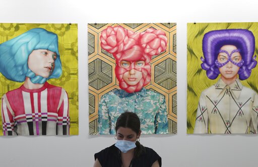 A gallery employee works in front of Angeles Agrela paintings at the 14th edition of Art Dubai at Dubai International Financial Centre, DIFC, which features 50 galleries from 31 countries with a focus on modern and contemporary art, in Dubai, United Arab Emirates, Tuesday, March 30, 2021. (AP Photo/Kamran Jebreili)