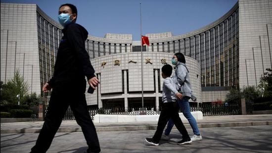 People wearing face masks walk past the headquarters of People's Bank of China. (REUTERS)