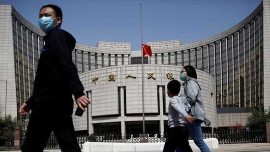 People wearing face masks walk past the headquarters of People's Bank of China. People wearing face masks walk past the headquarters of People's Bank of China.