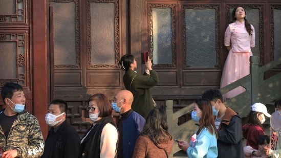 A woman poses for photos near visitors wearing face masks to protect against Covid-19 at the West Lake in Hangzhou on April 4. China got off to a slow start in vaccinating its population of 1.4 billion people, despite having four vaccines approved for general use, but has now rolled out a nationwide vaccination drive in an effort to build herd immunity.(Mark Schiefelbein/AP)