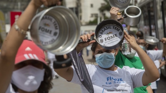 Residents of the Paraisopolis slum hold empty pots with the Portuguese phrase "Brazil goes hungry" to demand food aid for those affected economically by the pandemic, in Sao Paulo on April 5. Sao Paulo state, Brazil's most populous with 46 million residents, registered almost 1,400 deaths in the latest count. Health officials said the figure was partly due to the Easter holiday, which delayed the count, AP reported.(Andre Penner / AP)