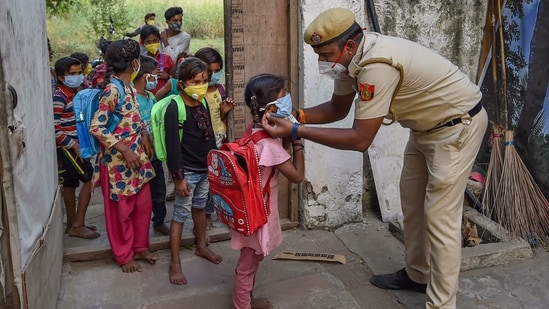 Delhi Police constable Than Singh, posted at Lal Qila Chowki of Kotwali police station area, adjusts the mask of a child as they arrive to attend classes at Red Fort parking, in New Delhi, Tuesday, Oct 20, 2020. (PTI)