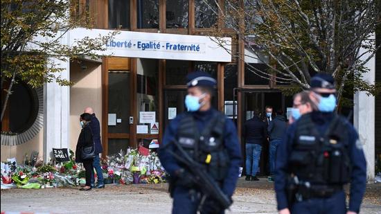 Police officers stand guard outside the Bois d'Aulne secondary school as people pay homage to slain history teacher Samuel Paty, who was beheaded by an attacker for showing pupils cartoons of the Prophet Mohammed in his civics class, on October 19, 2020, in Conflans-Sainte-Honorine, northwest of Paris. (AFP)