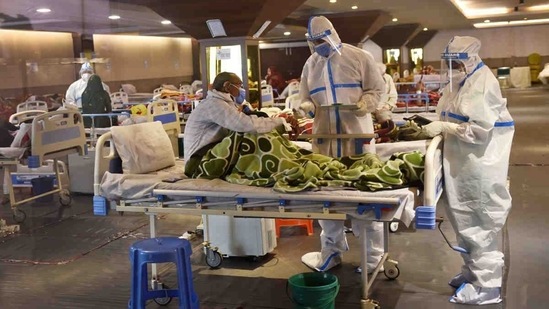Medical professionals in PPE coveralls tending to a patient at a temporary Covid Care facility in New Delhi on April 13. Chief minister Arvind Kejriwal, after a review meeting on April 12, directed state officials to increase the number of Covid-19 beds in the city. Later that day, the Delhi government converted 14 major private hospitals and six government hospitals into dedicated Covid-19 treatment facilities. (Ajay Aggarwal /  HT Photo)