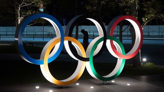 FILE - In this March 24, 2020, file photo, a man is seen through the Olympic rings installed near the National Stadium in Tokyo. (AP) FILE - In this March 24, 2020, file photo, a man is seen through the Olympic rings installed near the National Stadium in Tokyo. (AP)