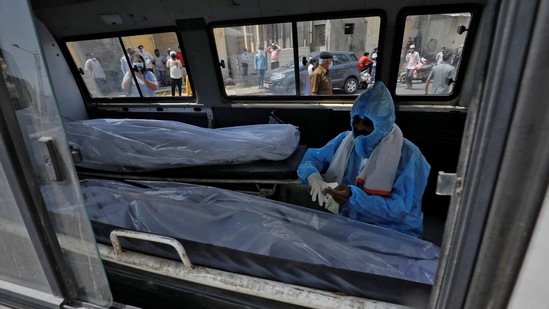 A man wearing a protective suit sits next to the bodies of the victims of the coronavirus disease (Covid-19) inside an ambulance at a mortuary of a hospital in Ahmedabad on April 15. The toll from the disease remained above 1,000 for the second day in a row with the addition of 1,038 fatalities on April 15.(Amit Dave / REUTERS)