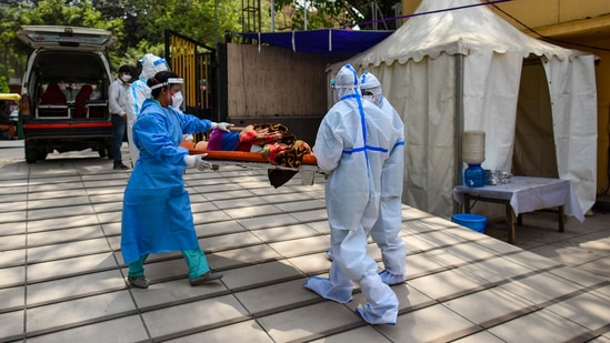 Health workers in PPE moving a Covid-19 patient to an isolation ward at a Covid care facility in New Delhi on April 16. Delhi has added the last 100,000 Covid-19 cases in eight days. In comparison, the previous 100,000 cases were registered over 120 days.(Amal KS / HT Photo)
