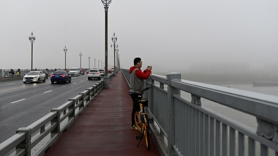 A commuter takes a picture from the Nanjing Bridge, in Jiangsu province, on April 2. Among the people Chen has saved, one was a young man who was particularly strong and bit through his tongue as several men dragged him from the bridge's edge, while another was a man who owed millions of yuan.(Wang Zhao / AFP)