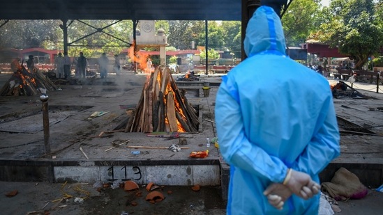A man in PPE coveralls looks on at pyres of Covid-19 victims, at Nigambodh Ghat crematorium, in New Delhi, on April 21.(Amal KS / HT Photo)