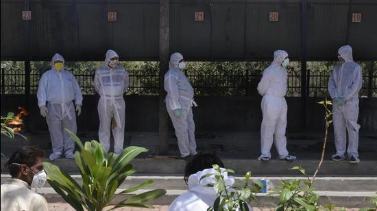 Relatives of a Covid-19 victim in PPE coveralls wait for the body at a crematorium in Sector 32, Gurugram, on Wednesday, April 21. (Vipin Kumar /HT photo)