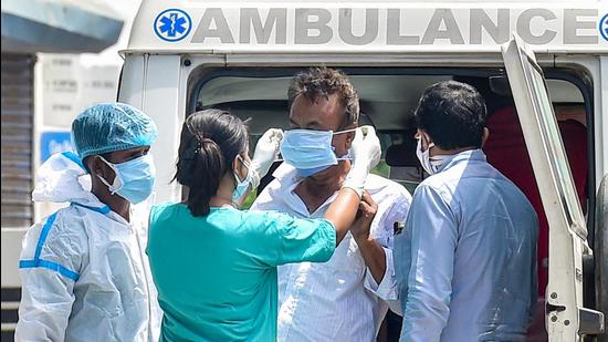 A healthcare worker helps a Covid-19 patient to wear a surgical mask after getting off an ambulance amid a countrywide spike in coronavirus cases. (PTI PHOTO.) A healthcare worker helps a Covid-19 patient to wear a surgical mask after getting off an ambulance amid a countrywide spike in coronavirus cases. (PTI PHOTO.)