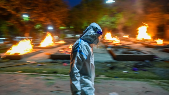 A man in PPE coveralls walks past funeral pyres of Covid-19 victims, at Sarai Kale Khan crematorium, in New Delhi, India, on Wednesday, April 28, 2021. (Photo by Amal KS/ Hindustan Times) A man in PPE coveralls walks past funeral pyres of Covid-19 victims, at Sarai Kale Khan crematorium, in New Delhi, India, on Wednesday, April 28, 2021. (Photo by Amal KS/ Hindustan Times)