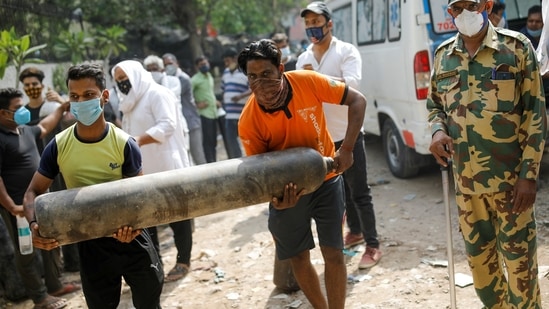 People carry an oxygen cylinder outside a factory to get it refilled in New Delhi on April 28. A second significant difference is likely to be when 48 pressure swing adsorption (PSA) medical oxygen generation plants begin functioning over the next month. By the end of April, officials may be better poised to increase critical care capacity, although this will depend on the evolution of the outbreak and if more turn critical.(Adnan Abidi / REUTERS)