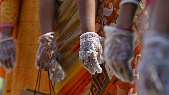 Voters wearing hand-gloves following Covid-19 protocols stand in a queue at a polling station to cast their ballot during the fifth phase of polling in Kolkata. As the election process meandeared through its course, the Covid-19 scourge that appeared to have been tamed in the initial stages began rearing its head.(Dibyangshu Sarkar / AFP)