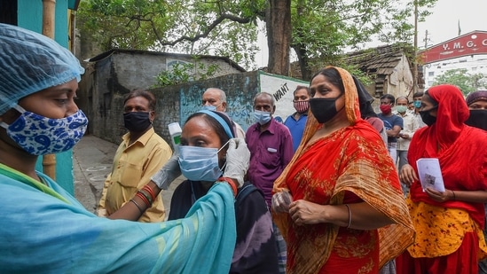 A health worker ties a face mask to a voter at a polling station during the sixth phase of polling at Khardha, in North 24 Parganas on April 22. As experts sounded an alarm while rival contenders for power held massive rallies where Covid-19 norms were flouted, the TMC knocked on the doors of the Election Commission for clubbing together the last three phases of polling but its request was turned down.(Ashok Bhaumik / PTI)
