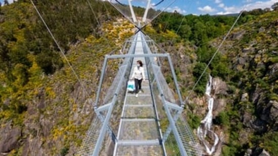 A woman walks across a narrow footbridge suspended across a river canyon, which claims to be the world's longest pedestrian bridge, in Arouca, northern Portugal, Sunday, May 2, 2021. The Arouca Bridge inaugurated Sunday, offers a half-kilometer (almost 1,700-foot) walk across its span, some 175 meters (574 feet) above the River Paiva.(AP)