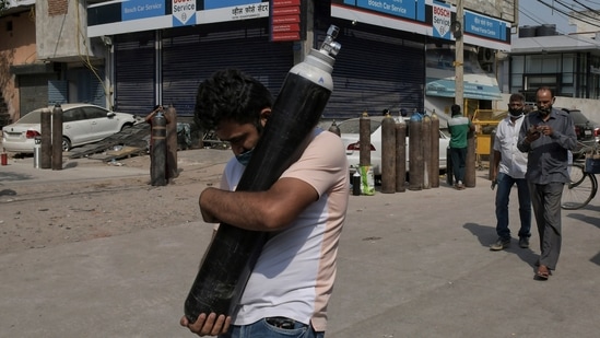 A man walks carrying a refilled cylinder as family members of Covid-19 patients wait in queue to refill their oxygen cylinders at Mayapuri area in New Delhi, India.(AP) A man walks carrying a refilled cylinder as family members of Covid-19 patients wait in queue to refill their oxygen cylinders at Mayapuri area in New Delhi, India.(AP)