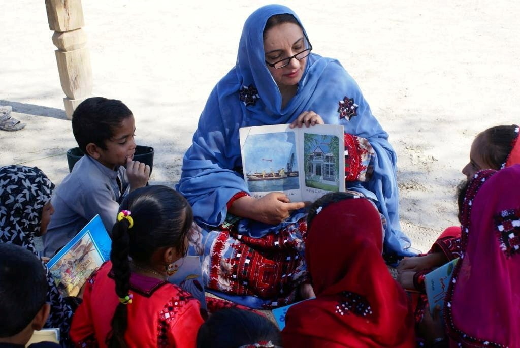 Children listen as a woman reads a book brought by Roshan the camel in Mand, Pakistan (via REUTERS)