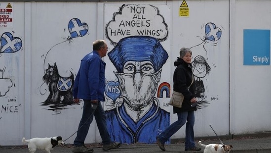 People are seen walking their dogs while passing a graffiti in support of the NHS, as the spread of the coronavirus disease (Covid-19) continues in Britain. (Reuters)