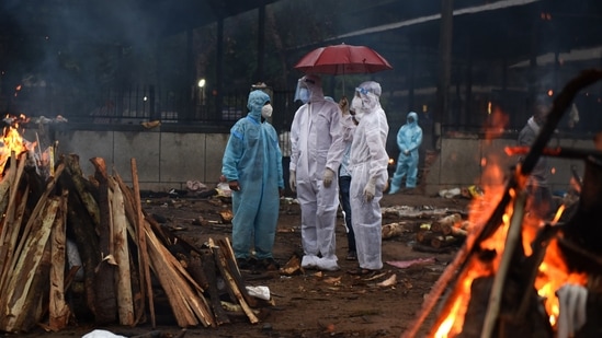 Relatives of a Covid-19 victim seen under an umbrella as it rains during a mass cremation in Seemapuri, New Delhi on May 6. According to a new analysis from the University of Washington’s Institute for Health Metrics and Evaluation (IHME), the Covid-19 pandemic has caused nearly 6.9 million deaths across the world, more than double the number officially recorded, Reuters reported.(Ajay Aggarwal / HT Photo)