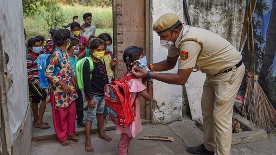 Delhi Police constable Than Singh, posted at Lal Qila Chowki of Kotwali police station area, adjusts the mask of a child as they arrive to attend classes at Red Fort parking, in New Delhi. (PTI) Delhi Police constable Than Singh, posted at Lal Qila Chowki of Kotwali police station area, adjusts the mask of a child as they arrive to attend classes at Red Fort parking, in New Delhi. (PTI)